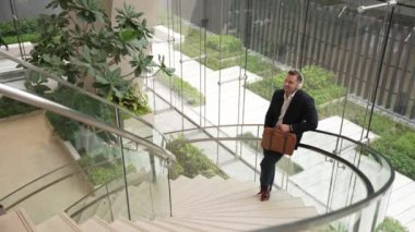 Kafkasyalı iş adamının, modern binadaki spiral merdivenlerde dikilirken kulaklık takıp rahatlatıcı müzik dinlemesinin en üst görüntüsü. Proje yöneticisi kafiyeye geçerken şarkıyı dinlemeyi sever. Urbane.