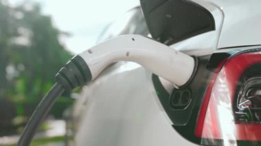 Yavaş çekim EV elektrikli araba yazın yeşil sürdürülebilir şehir bahçesinde şarj oluyor. Kentsel sürdürülebilirlik yaşam tarzı yeşil temiz yeniden şarj edilebilir enerji elektrikli BEV araç iç organları