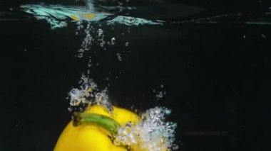 Suda yüzen sarı dolmalık biberi kapat. Biber yuvarlaktır ve üzerinde yeşil bir sapı vardır. Suya düşen sarı dolmalık biber ve siyah arkaplan. Pabulum.