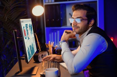 Zeki iş adamı satış ekibiyle uzaktan tanışıyor, gözlüklü kameraya bakıyor iş grafiği araştırma hedef pazarı ile birlikte Neon Dark Light Home Office 'deki bilgisayar ekranında ürün veritabanında. Tahmin et..