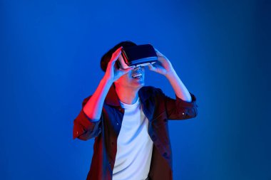 VR 'a bakan Asyalı adam, ilginç nesne teknolojisi üzerine fantastik meta-meta izlemeyi seviyor. Sanal gerçeklik üzerine mavi neon ışıklandırma arka planı. Üç boyutlu hologram yeniliğinde yeni dünya. Entrika.