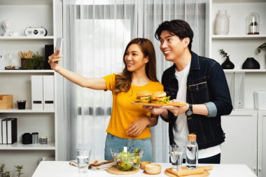 Gülümseyen sunucu şefler akıllı telefonla selfie çekerek sosyal medya kanalından canlı yayında yemek programında çift büyük hamburger yapıyorlar. İnfobahn.