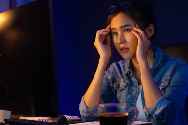 Stresli, genç, güzel Asyalı yaratıcı proje yaratıcısı sosyal medyayı araştırmak için bilgisayara bakıyor ve geceleri daha çok neon modern ofisin planlama kanalı stratejisine ulaşılıyor. Taktik.