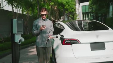 Yavaş çekim adamı, uygulama ekranında elektrikli araba aküsü şarj durumu, menzil ve şarj limitini kontrol ediyor. Akıllı teknoloji aygıtı, EV arabasının araba aküsündeki elektrik depolama verilerini şarj ettiğini gösteriyor..
