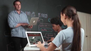 Afrikalı erkek manken tamir ederken beyaz kız programlama ya da kodlama sistemi. Öğretmen elinde dizüstü bilgisayar tutarken çeşitli çocukların web geliştirme programı yazmalarına bakıyor. Yenilik eğitimi. Öğretim