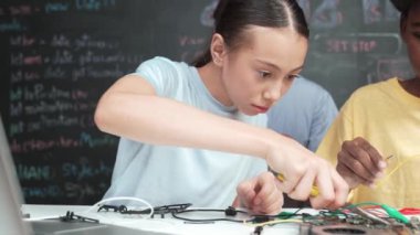 Çeşitli öğrenciler elektronik alet tamir tahtasını kullanırken, beyaz öğretmenler de STEM teknoloji sınıfında robot araba hazırlamaya yardım ediyor. Kablo ve anakart kullanarak çalışan çok kültürlü insanlar. Öğretim