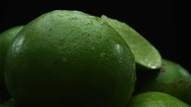 Limon dilimleri titizlikle bir yığın halinde, siyah arkaplana göre dizilmiş. Her bir kireç dilimi çarpıcı detaylar, canlı yeşil rengi ve baştan çıkarıcı dokusu ile yakalanır. Kapatın. Geliştirilebilir.