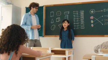 Öğrenciye bakan beyaz bir öğretmen kendini karatahtaya tanıtıyor. Çeşitli öğrenciler karatahtaya bakarken sınıfın önünde duran çekici kız. Eğitim konsepti. Pedagoji.