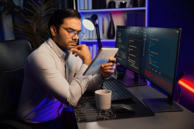 Akıllı bilişim geliştiricisi bilgisayar ekranında yazılım geliştirme kodlaması üzerinde çalışıyor ve en yeni uygulama projesinin notlarını okuyor, program güncellemesi düşünüyor neon ışıklı siber ofiste online web sitesi verileri. Tahmin et..