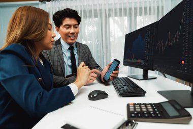 Gülümseyen işadamı cep telefonundaki dinamik borsa verilerini, iç ofisindeki internet sitesi uygulamasını analiz etmek için not yazan kadınlara gösteriyor. İnfobahn.