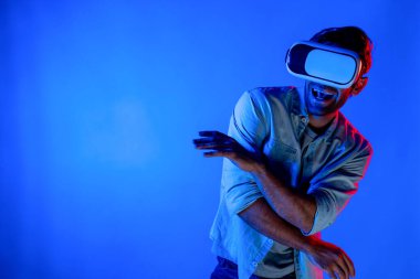 Yakışıklı, dans eden ve müziğe hareket eden bir adam. VR gözlüğü ve neon ışıklı arka plan kullanarak. Beyaz erkek oyuncu, teknolojik yenilikler giyerek pop müzik dinlerken ayakta duruyor. Sapma.