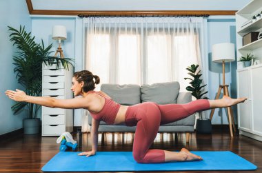 Spor kıyafetleri içinde esnek ve becerikli bir kadın evde egzersiz paspası üzerinde meditasyon pozisyonunda yoga yapıyor. Huzurlu ve huzurlu bir yoga yaşam tarzı..