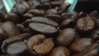 Makro kahve çekirdekleri kamerayla kaşığa saçılıyor. Beyaz kaşık kepçesiyle kahverengi kahve çekirdeklerini kapayın ve siyah arkaplanla dağılın. Kafein enerji içeceği konsepti. Pabulum.