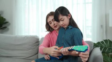 Kafkasyalı bir anne evde akustik müzik öğretirken ukulele çalan mutlu kız. Sevimli çocuk enstrüman öğreniyor. Kafkasyalı mutlu anne ve kız birlikte vakit geçiriyorlar. Pedagoji.