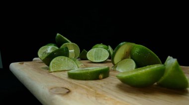 Yakın plan, canlı bir dilim taze kireç kırsal bir ahşap kesme tahtasının üzerinde duruyor. Tazelik ve canlılık yayıyor. Kesme tahtasına konmuş yeşil limon diliminin yarı saydam zarları. Geliştirilebilir.