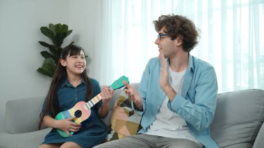 Caucasian father clapping hand to motivated and encouraged while smart daughter playing ukulele at living room. American girl learning guitar while show to her dad. Family creation concept.Pedagogy. clipart