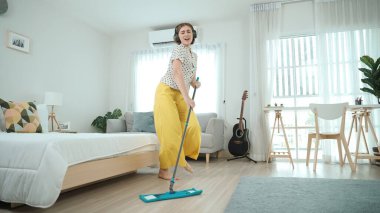 Gülümseyen kulaklıklı hizmetçi yerleri temizlerken müzik dinliyor. Oturma odasında dans ederken yerleri paspaslayan Kafkasyalı mutlu bir anne. Gülümseyen anne ev işi yapıyor. Yaşam tarzı. Pedagoji