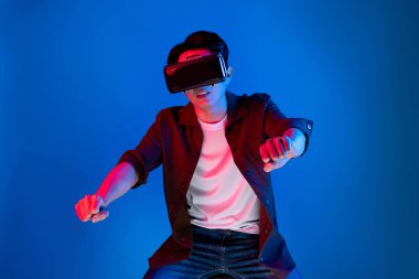 VR kullanan zeki bir oyuncu araba yarışlarında araba sürerken yeni dünyaya dönüyor mavi neon ışıklı duvar bağlantılı fütüristik teknoloji sanal gerçeklik meta 'sını izole ediyor. Entrika.