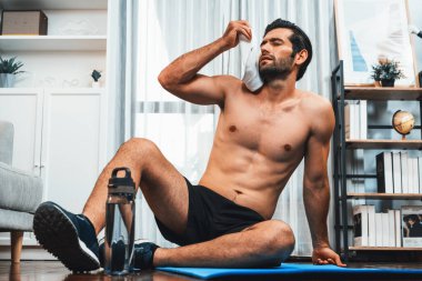 Sporcu ve atletik bir adam evde vücut egzersizlerini bitirdikten sonra spor minderinde dinleniyor. Formda ve sağlıklı bir yaşam tarzı için. Gaiety evde egzersiz eğitimi.