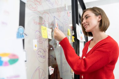 Profesyonel çekici kadın lider, modern iş toplantılarında beyin fırtınası yaparak zihin haritalama istatistikleri kullanarak yaratıcı pazarlama planını sunarken yapışkan bir nota yapıştırıyor. Tertemiz..