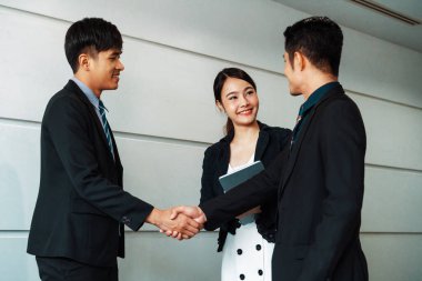 İş adamları konsepti kabul ediyor. İş adamı toplantı odasında başka bir iş adamıyla tokalaşıyor. Genç Asyalı sekreter bayan onların yanında duruyor. uds