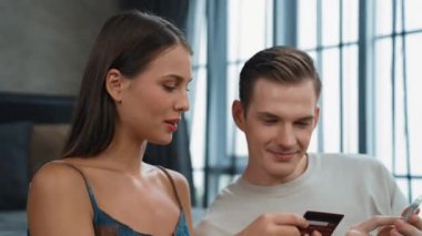 Genç çift, kredi kartıyla ödemek için internet üzerinden ödeme uygulaması ve dijital cüzdan kullanarak yatak odasında oturuyor. Mobil internet üzerinden alışveriş ve modern alımlar. Düzenle