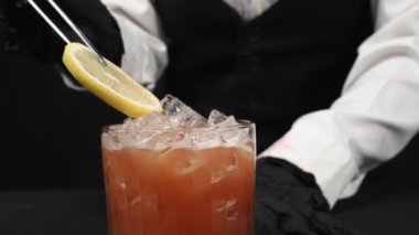 Dilimlenmiş limonlu tekila kokteyli ile süslenmiş barmen elini kapat. Yetenekli barmen Macro kokteyl servisi için hazırlanıyor ve tazelenmesi için narenciye ile süsleniyor. Geliştirilebilir.