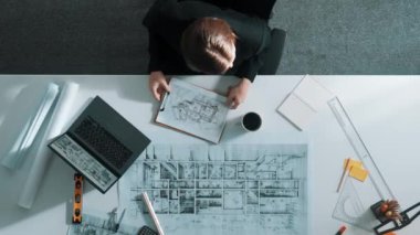 Yöneticinin proje planı, ekipman ve güvenlik kaskıyla toplantı masasında otururken projeye bakışının üst görüntüsü. Ev tasarımını incelerken planlara bakan mühendislerin hava görüntüsü. Hizalama.