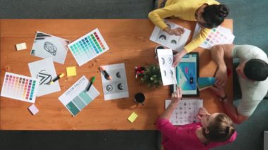 Proje yöneticisi renk paletleri seçerken tasarımcının tablete baktığı yukarıdan aşağıya hava görüntüsü. Profesyonel grafik tasarımının en üst görüntüsü ve logoya bakın. Yetenekli ekip grafikleri seçiyor. Sempozyum.