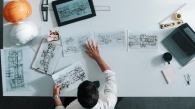 Proje planını kontrol ederken ve seçerken mimar mühendisin bina planlarını masaya yerleştirdiği tepeden aşağı hava görüntüsü. İç mimar toplantı masasından mimari plan seçti. Hizalama.