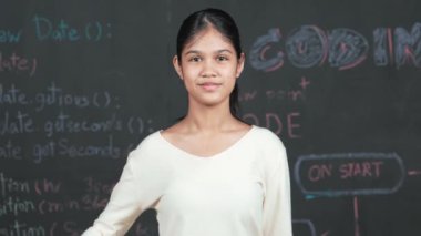 Genç öğrenci başarılı planını kutlarken kolunu kaldırdı. Mühendislik koduyla karatahtaya bakarken kameraya bakan mutlu genç, STEM sınıfında yazılı. Öğretim