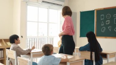 Çeşitli öğrenci ödevlerini kontrol ederken etrafta dolaşan ve etrafa bakan beyaz bir öğretmen. Çok kültürlü çocukların okuması ve dinlemesi ilkokuldaki sınıfta fikrini açıklıyor. Pedagoji.