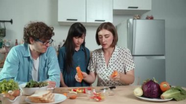 Çekici beyaz anne ve baba Asyalı kızıyla taze yemek pişirmek için birlikte vakit geçiriyorlar. Enerjik anne ve baba mutfakta salata yapmak için taze sebze hazırlıyor. Sağlıklı yiyecekler. Pedagoji.