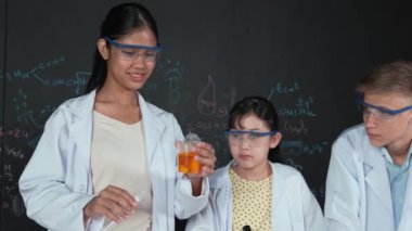 Değişik öğrenciler masada mikroskop ya da tüpü sıvıyla karıştırırken renkli solüsyonları karıştırıyorlar. Kimyasal teorisiyle karatahtanın önünde duran Asyalı kız deney tüpü tutuyor. Öğretim