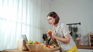 Kafkasyalı anne, modern mutfakta dizüstü bilgisayarda yemek tarifine bakarken salata yapmak için yemek hazırlıyor. Yetenekli ev bekçisi taze sebze kullanarak kahvaltı hazırlıyor. Pedagoji.