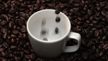 Kahve fincanının içine kahve çekirdeği yığını ile çevrili bir şekilde düşüyor. Beyaz fincana aromatik fasulye döküyorum. Kahvenin üst görüntüsü siyah arka planlı cama düşer. Geliştirilebilir.