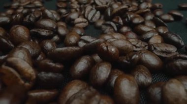 Karışık aromalı kahve çekirdeği yığını masaya saçılmış ve kavrulmuş kahve çekirdekleri etrafa saçılmış siyah arkaplanla çevrilmiş. Makrografi. Ağır çekim. Pabulum.