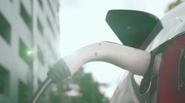 Yavaş çekim EV elektrikli araba yazın yeşil sürdürülebilir şehir bahçesinde şarj oluyor. Kentsel sürdürülebilirlik yaşam tarzı yeşil temiz yeniden şarj edilebilir enerji elektrikli BEV araç iç organları