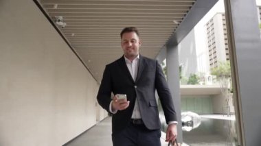 Happy proje yöneticisi koridorda yürürken cep telefonunu kontrol ediyor. Profesyonel iş adamı başarılı projesini kutlarken ya da satışları artırırken takım elbise giyer ve bavulu toplantı için tutar. Urbane.