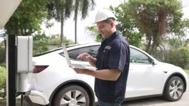 Evde EV şarj istasyonu kurulumu üzerinde çalışan nitelikli teknisyen, EV için dizüstü bilgisayarla şarj sisteminde sorun çıkarma ve yapılandırma ayarları yapıyor. Titiz