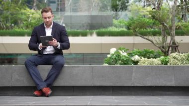 Kafkas akıllı işadamı tablet kalem kullanarak ve pazarlama stratejisi planlayarak parkta oturuyordu. Yönetici finansal planı düşünürken veri analizine bakıyor. Urbane