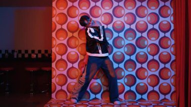 Asyalı break dansçı serbest stile geçiyor ve balon arka planlı kameraya bakıyor. Profesyonel hippi gündelik kıyafet giyer ve gözlük takar. Mutluluk.