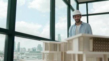 Gökdelen manzarasına bakarken yürüyen profesyonel mimar mühendisi. Masaya yerleştirilmiş ev modeliyle pencereye bakarken yetenekli proje yöneticisi proje planını tutuyor. Tasarım. İzleme