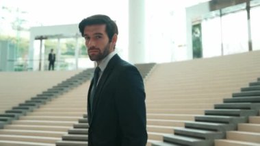 Akıllı iş adamı merdivenlerde kameraya bakıyor. İş elbisesi giyerken kameraya gülümseyen başarılı adamın yakın çekimi. Yönetici, kameraya bak. Hareket eden kamera. Sevinçli..