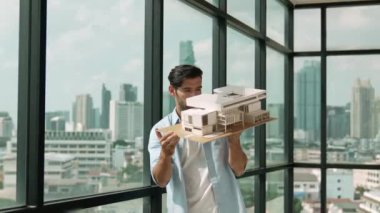 Yetenekli gülümseyen beyaz mühendis hata noktasını kontrol etmek için ev modelini sağa sola çeviriyor. Profesyonel yönetici teftiş, kontrol, mimari modele bakmak. Tasarım konsepti. İzleme