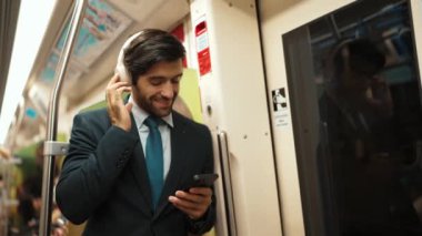 Akıllı yönetici trende dururken kulaklık takar ve müzik dinler. Profesyonel iş adamı, şarkıları dinlerken ve şarkı seçerken bölüme yaslanıyor. İş konsepti. Sevinçli..