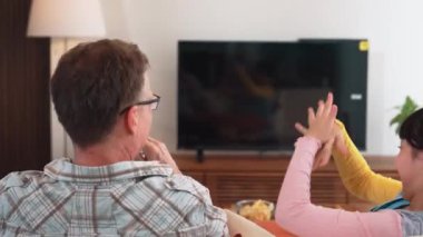 Grandfather and granddaughter eat french fries watch interesting entertainment on TV. Senior use technology communicate with young generation cross generation gap strengthen family bond. Divergence.