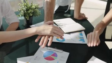 Becerikli pazarlama ekibi, şehir manzaralı iş toplantı odasında dökümanlarla el ele tutuşuyor. İş adamları başarıyı kutluyor. İşbirliğini, birliğini temsil etti. İzleme