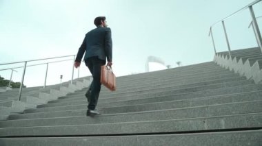 Akıllı bir iş adamının elinde çantayla merdivenlerden yukarı çıkışının en üst görüntüsü. Profesyonel proje yöneticisi merdivenlerden çıkıp işyerine gidiyor. Yeteneklerini arttırmak, terfi almak, seyahat etmek. Sevinçli..