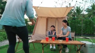 Aile hep birlikte bahçedeki kampta oturup yemek yiyor. Ebeveynler, genç nesil arasında iletişim kurmak ve zaman geçirmek için açık hava kamp faaliyetlerini kullanıyorlar. Uyumsuzluk.